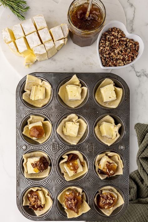 antique muffin pan filled with unbaked brie bites, topped with fig jam and walnuts Brie Bites Puff Pastry Fig, Fig And Brie Bites, Fig Brie Bites, Appetizers Using Fig Jam, French Onion Brie Puffs With Fig Jam, Baked Brie With Fig Jam Puff Pastry, Brie Fig Jam Appetizer, Baked Brie And Fig Jam, Fig Brie Puff Pastry