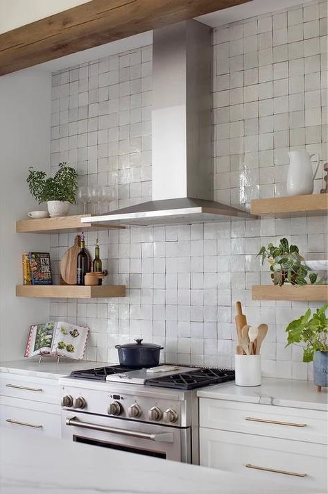 A stainless steel range hood is mounted to gray glazed backsplash over a stainless steel oven range and between stacked oak floating shelves. Kitchen Shelves Around Hood, Open Shelf Upper Cabinets, Floating Shelves By Range Hood, Hood Range With Open Shelves, Tile Behind Range Hood Open Shelves, Range Hood Shelving, Oven Hood With Open Shelving, Stove With Floating Shelves, Extractor Hood Ideas Open Shelves