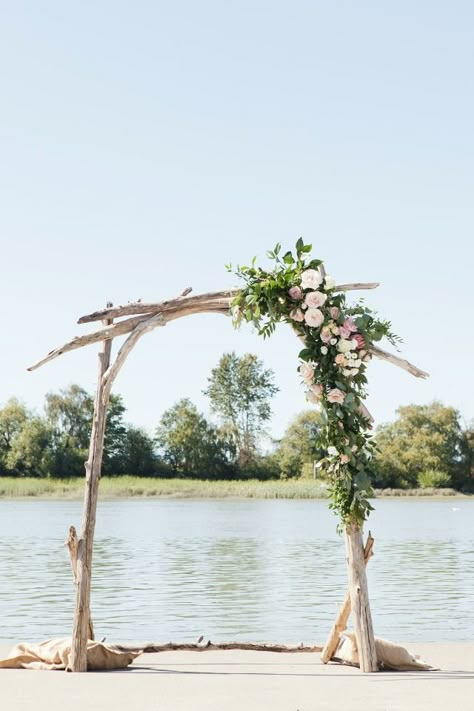 driftwood wedding arch with asymmetrical flower accent Driftwood Wedding Arch Diy, Driftwood Wedding Altar, Driftwood Alter Wedding, Natural Wood Arbor, Driftwood Wedding Arbor, Asymmetrical Wedding Arch Flowers, Driftwood Arbor Wedding, Drift Wood Wedding Arch, Lake Wedding Arch