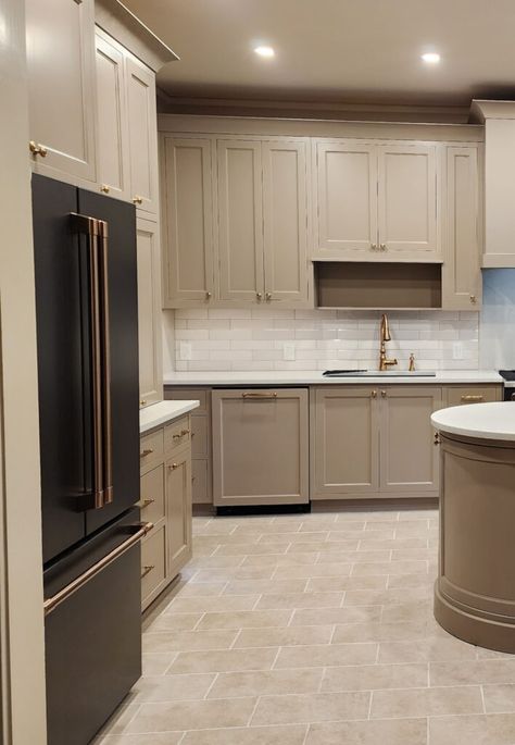 Shown here, a medium-toned mushroom (greige-beige-taupe) kitchen with painted cabinets, travertine-look tile floor, subway tile backsplash and white quartz countertop with GE Cafe Matte Black appliances, fridge has brushed brass hardware. Gold faucet.   #kyliem #kitchenremodel #paintedcabinets #diy #homeupdate Mushroom Grey Kitchen Cabinets, Gray Cabinets White Subway Tile, Small Kitchen Taupe Cabinets, Brown Taupe Kitchen Cabinets, Tan Beige Kitchen Cabinets, Backsplash Kitchen Greige Cabinets, Kitchen Cabinet Colors With White Quartz, Neutral Kitchen With Granite, Oak And Taupe Kitchen