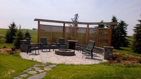 Amazing fire pit area with cedar wind wall and seating wall and pillars surrounding the pad. Van Tryp Residence Privacy Around Fire Pit, Fire Pit Privacy Wall, Privacy Fire Pit Ideas, Lattice Privacy Screen Fire Pit, Privacy Wall Fire Pit, Fire Pit With Privacy Wall, Fire Pit Privacy Ideas, Acreage Ideas, Paver Fire Pit