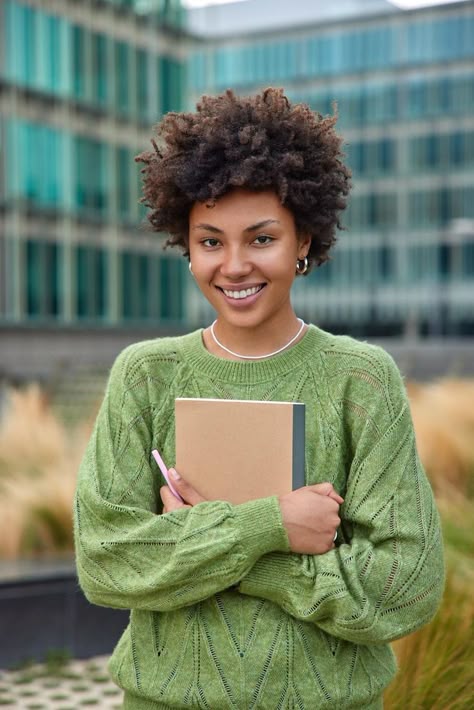 Free Photo | Vertical shot of happy young woman with curly hair holds notepad and pen makes notes what she observes around in city dressed in casual green jumper poses outdoors against blurred background Notepad And Pen, Woman With Curly Hair, Africa Art Design, Green Jumper, Short Box Braids Hairstyles, Diverse People, Blurred Background Photography, Green Jumpers, Illustration Story