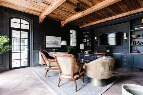 In the office, a wall-mounted TV screen all but disappears against near-black grasscloth wallpaper. Intricately laid wood flooring and a ceiling clad in reclaimed oak adds warmth and contrast to the room’s dark walls, painted with Sherwin-Williams‘ Iron Ore. Photo by Rebekah Westover. Moody Office Design, Moody Office, Utah Style, Walnut Floors, Industrial Floor Lamps, Wood Ceiling, Modern Office Chair, Industrial Flooring, Curved Staircase