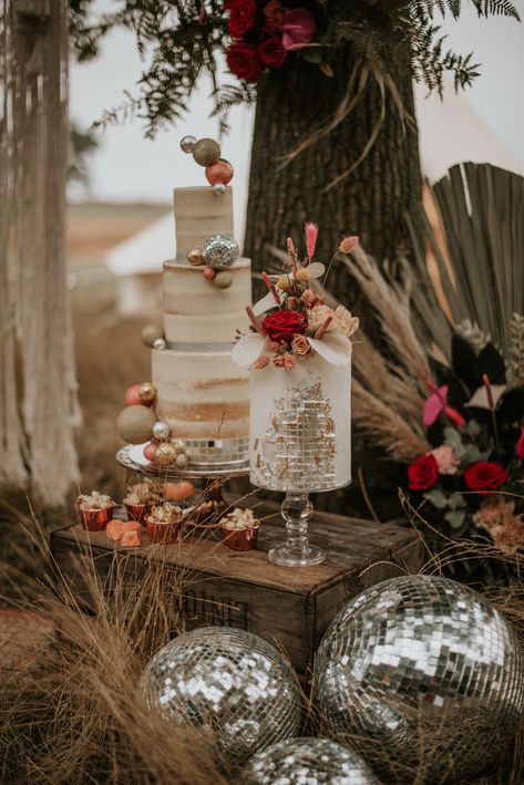 This shows images of a cake display at an outdoor wedding. There are two cakes, one three-tiered cake and a single layer cake, both on glass vintage cake stands. The cakes are displayed on a crate. At the base of the crate are differently sized silver disco balls. Behind the cake display are dried flower arrangements. Pampas Disco Wedding, Boho Disco Wedding Cake, Groovy Wedding Cake, Disco Ball Wedding Cake, Disco Cake Pops, Disco Wedding Cake, Boho Disco Wedding, Wedding Disco Ball, Disco Ball Cake