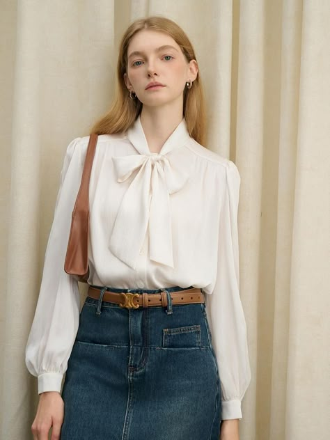 This product is a refined dove ribbon blouse, designed with a delicate tie at the neck that adds a touch of femininity to the piece. The blouse features billowy sleeves that taper into fitted cuffs, and the lightweight fabric offers a comfortable, airy feel. With its pleated detailing and elegant drape, this blouse is a timeless addition to any professional or dressy ensemble. - The blouse showcases a charming ribbon tie at the neckline, allowing for a customizable bow that can be styled to suit any occasion.- Billowing sleeves with buttoned cuffs add an element of classic sophistication to the garment's design.- Pleated accents run the length of the blouse, providing texture and visual interest.- Crafted from a light, flowing fabric, the blouse promises comfort and ease of movement t Bow Tie Blouse Outfit, White Wrap Blouse, Ribbon Blouse, Korean Blouse, Fashion Design Books, Frilly Blouse, Bow Tie Blouse, Billowy Sleeves, Maxi Outfits