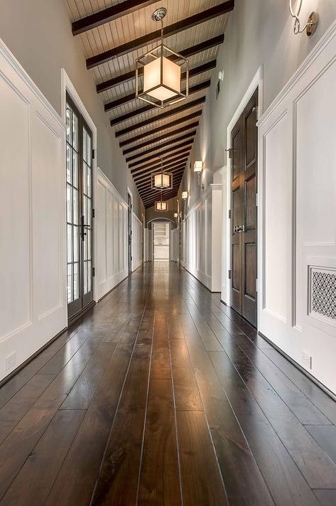 Gorgeous hallway features a sloped ceiling dotted with dark stained wood beams and caged Lanterns with Paper Shades. Stained Wood Beams, Houses Inside, Luxury Farmhouse, Hallway Ceiling, Long Hall, Pole House, Hall Lighting, Entryway Lighting, Dark Wood Stain