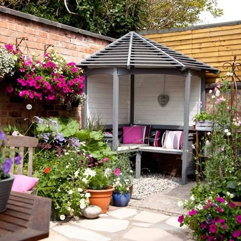 This small, walled courtyard garden has been turned into an ideal summer retreat perfect for socialising and relaxing. The eye is immediately drawn to the charming grey and cream painted arbour come summer house. Pretty hanging baskets and pots bursting with pink petunias pick out the fuchsia scatter cushions within the inviting space Walled Courtyard Garden, Small Courtyard Gardens, Courtyard Gardens Design, Corner Garden, Small Courtyards, Garden Gazebo, Diy Outdoor Decor, Garden Pictures, Garden Seating