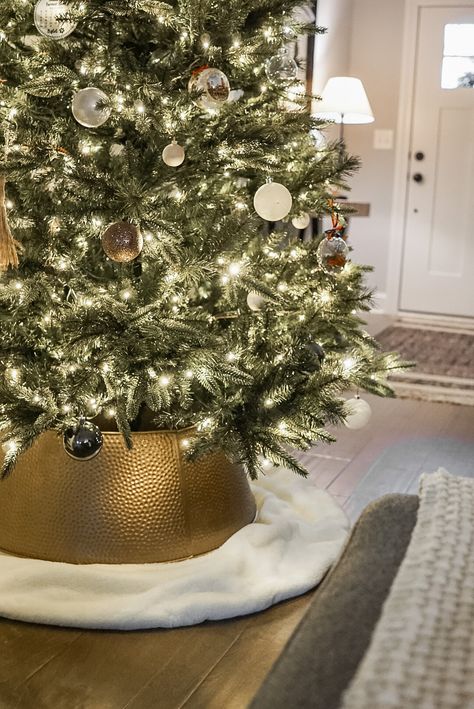 Looking for an affordable dupe to the Crate and Barrel Bash Gold Tree Collar? This post is for you! Christmas Tree. Tree Collar. DIY. Designer Dupe. Studio Mcgee. Crate and Barrel. Mcgee and Co. Spray Paint. Mini Golden Bead Garland. Bells. Ornaments. Neutral. Black Christmas Tree Collar, Velvet Tree Collar, Gold And Wood Christmas Tree, Tree Collar Vs Tree Skirt, Crate And Barrel Christmas Decor, Diy Tree Collar Christmas, Brass Christmas Tree Collar, Christmas Tree Collar Ideas Diy, Gold Tree Collar