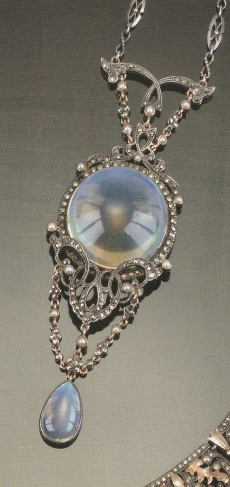 AN ARTS AND CRAFTS MOONSTONE, MARCASITE AND HALF-PEARL PENDANT. Centred on a circular cabochon moonstone with silver scroll mounts and garland chains to a drop-cut moonstone drop, on a chain, apparently unmarked. Source: Christie's 20th Century Jewellery, 12 October, 2000. #ArtsAndCrafts Vintage Statement Jewelry, Tiaras Jewellery, Marcasite Jewelry, Edwardian Jewelry, 12 October, Unusual Jewelry, Moonstone Jewelry, White Gold Jewelry, Gothic Jewelry