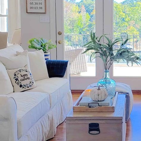 Rectangular light wood trunk coffee table is paired with a stained wood decorative tray. The table stands in front of white French patio doors in this white sofa living room. White Sofa Living, White Farmhouse Living Room, Shiplap Living Room, Sofa With Coffee Table, Farmhouse Living Room Curtains, White Sofa Living Room, French Patio Doors, Dark Wood Coffee Table, Coffee Table Decor Tray