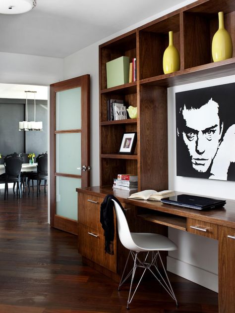 In this home office, which has gorgeous dark wood floors, a wood desk is paired with a built-in shelving unit, used to display two yellow vases, several books, a framed picture and other accessories. A midcentury modern white chair offers a place to sit. Home Office Built Ins With Desk, Home Office With Built Ins, Built In Desk And Shelves, Canvas Workspace, Dark Wood Desk, Minimalist Spaces, Home Office Built Ins, Office Built Ins, Storage Inspiration