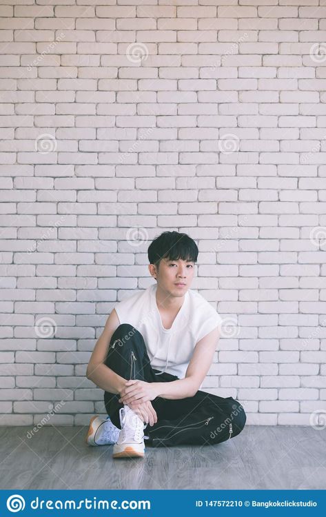 Photo about Asian model man in black pants and white shirt sitting on floor and knee up, photo shot on white bricks wall background. Image of adult, concept, asia - 147572210 Man Sitting On The Floor Reference, Man Sitting On Floor Pose Reference, Guy Sitting Side View, Sitting Reference Pose Floor, Guy Sitting On Floor, Man Sitting On Floor, Sitting Photography, White Bricks, Guy Sitting