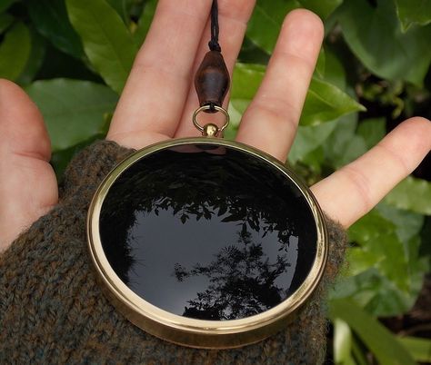 A round brass frame surrounding black glass with a vintage wooden bead and hemp cord. Mirror Scrying, Black Scrying Mirror, Witchcraft Tools, Altar Pieces, Dr Script, Scrying Mirror, Mirror Pendant, Divination Tools, Hemp Cord