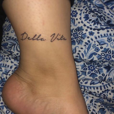 Ankle tattoo in cursive font that reads “Della Vita” Name On Ankle Tattoo, Cursive Ankle Tattoo, Tattoo In Cursive, Tattoo Around Ankle, Tat Fonts, Cursive Name Tattoo, Tattoo Fonts Cursive, In Cursive, Cursive Font