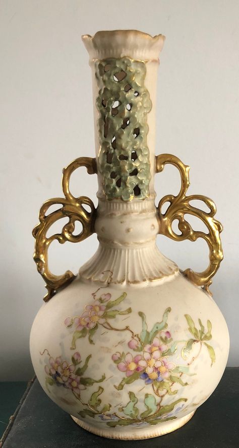 Antique vase by Wien Teplitz, made in Austria. Approximately 8 inches in height. It has a cream background with gilded handles and hand painted flowers in soft pink and green with gold accents. The top portion of the vase is pierced. The back stamp for the company (pictured) dates it to the early 20th century.  Please note there is some wear to the gilding on the handles and a small nick along the bottom rim. This vase has been used (please see the photo showing the inside.) Lovely and delicate. Fantasy Vase, Antique Vases Vintage, Vases Antiques, Vintage Vessel, Green With Gold Accents, Victorian Vases, Amphora Vase, Antique Vases, Old Vases