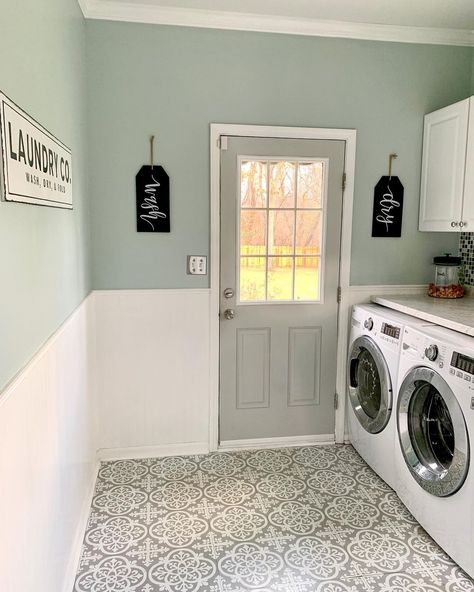 Gray door is fitted into a light green wall with white beadboard wainscoting. A white washer and dryer are placed next to the door in this laundry room featuring white and gray mosaic flooring. Seafoam Green Laundry Room, Eucalyptus Laundry Room, Laundry Room Gray Walls, White Cabinets In Laundry Room, Pale Pink Laundry Room, Soft Green Laundry Room, Laundry Room With Beadboard, Laundry Room Ideas Wallpaper Accent Wall, White Beadboard Laundry Room