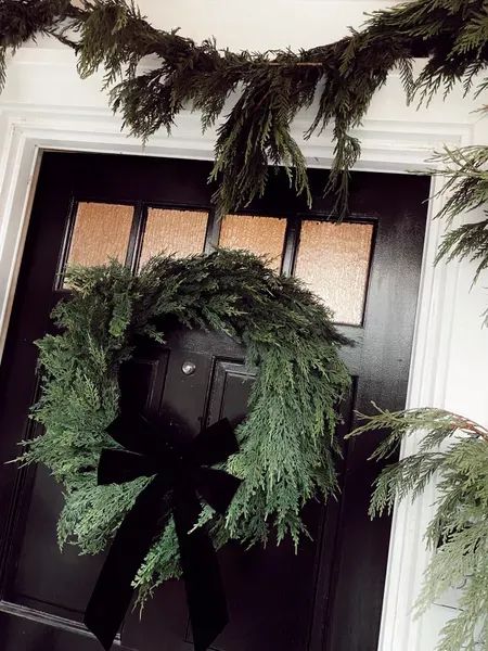 This realistic looking faux cedar wreath from Anthropologie pairs so perfectly with this black velvet bow from Target and gives our home a festive but sophisticated look. | holidays, festive, wreath, home, decorations, decor, house Black Door Christmas Decor, Moody Christmas, Xmas Market, Dolly Christmas, Cedar Wreath, Black Wreath, Black Velvet Bow, Christmas Planters, Festive Wreath