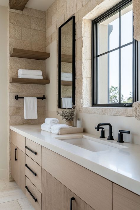 Modern bathroom with a stone wall, light wood cabinets, dark fixtures, and neatly folded white towels. Spanish Modern Bathroom, Black Hardware Bathroom, Modern Organic Bathroom, Bathroom Flip, Organic Bathroom, Organic Modern Bathroom, Earthy Bathroom, European Bathroom, Bathroom Elegant