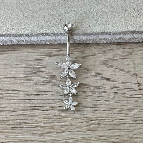 Elevate your belly button ring collection with this enchanting dangly silver belly button piercing, adorned with three exquisite CZ flowers.  Made with 316L Surgical Steel, this eye-catching piece is designed to catch the light and steal the spotlight. Whether you're dressing up for a night out or adding a touch of flair to your everyday look, this stunning belly button jewelry promises to be the perfect accessory.  Embrace elegance and individuality with this irresistible piece of navel jewelry Silver Belly Button Piercing, Dangle Belly Button Piercing, Belly Button Rings Dangle, Gold Belly Button Rings, Floral Minimalist, Bellybutton Piercings, Belly Button Piercing Jewelry, Button Piercing, Belly Button Jewelry