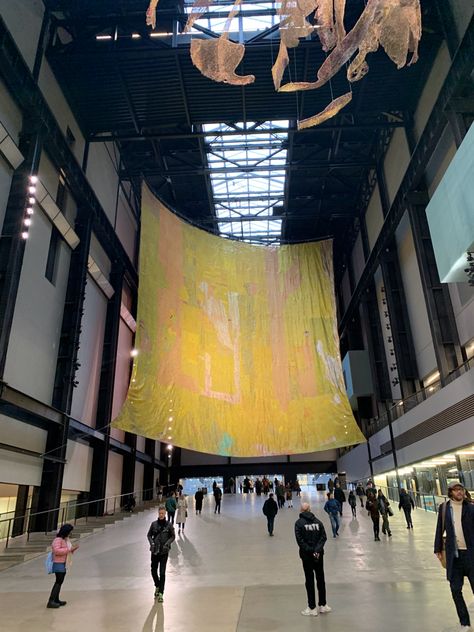 Photograph of El Anatsui’s installation in the Turbine Hall, Tate Modern, London (UK). The piece large installation is hanging from the ceiling, and is a fabric-looking metal sheet made of predominantly yellow-coloured, recycled bottle tops. Ghanaian Art, El Anatsui, African Photography, Turbine Hall, Tate Modern London, Contemporary African Art, London Look, Photography Exhibition, Art Exhibitions