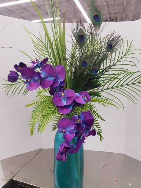 Orchids and peacock feathers Peacock Vase Arrangement, Centerpieces With Peacock Feathers, Peacock Arrangements Ideas, Arrangements With Peacock Feathers, Flowers With Peacock Feathers, Peacock Feather Arrangements, Peacock Feather Flower Arrangements, Peacock Feather Decor Ideas, Peacock Floral Arrangements