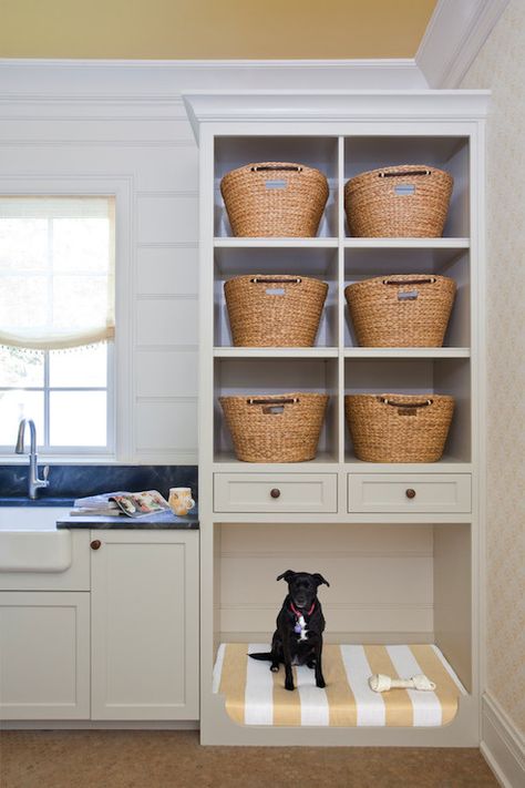 Fantastic cottage laundry room features white cabinets paired with soapstone countertops framing apron sink paired with gooseneck faucet and tongue and groove backsplash situated next to built-in shelves filled with woven laundry sorters stacked over built-in dog bed lined with white and yellow striped cushion atop terracotta hex tiled floor. Built In Dog Bed, Cottage Laundry Room, Laundry Room Storage Shelves, Laundry Room/mud Room, Rustic Laundry Rooms, Small Laundry Room Organization, Room Storage Diy, Farmhouse Laundry Room, Laundry Room Cabinets