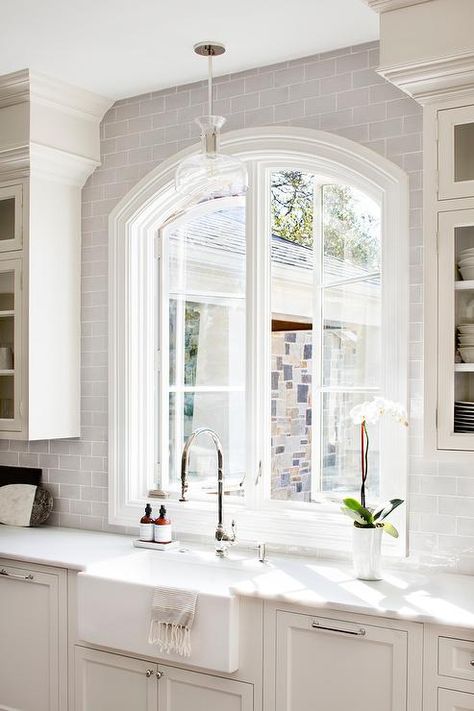 An arched casement window is framed by glazed gray backsplash tiles and lit by a clear glass pendant hung over a farmhouse sink fitted with a polished nickel gooseneck faucet. Backsplash Window, Kitchen Wall Tiles Backsplash, Modern Kitchen Pendants, Above Kitchen Sink, Gray Tile Backsplash, Kitchen Sink Window, Tiles Backsplash, Grey Backsplash, Kitchen Wall Tiles