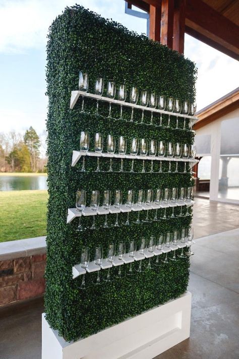 A faux greenery wall on a white base with white shelves holding champagne flutes. Branded Party Decor, Event Party Decor, Outside Event Decor, Business Party Decorations, Grand Opening Party Ideas Business, Upscale Party Decor, Corporate Birthday Party, Opening Ideas Events, Work Event Decor