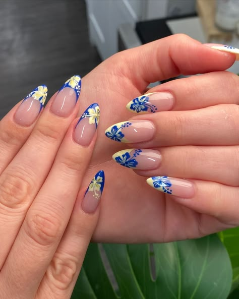 Almond-shaped nails with blue and yellow floral designs on a nude base, showcasing trendy, tropical-inspired nail art. Cute Beach Nail Designs, Summer Nails Crazy, Nail Into Summer, Nail Inspo Hibiscus Flower, Summer Tips Nails, Nail Inspo Trendy Blue, Blue French Tip Nails With Flower, Nail Yellow Design, Blue And Yellow Summer Nails