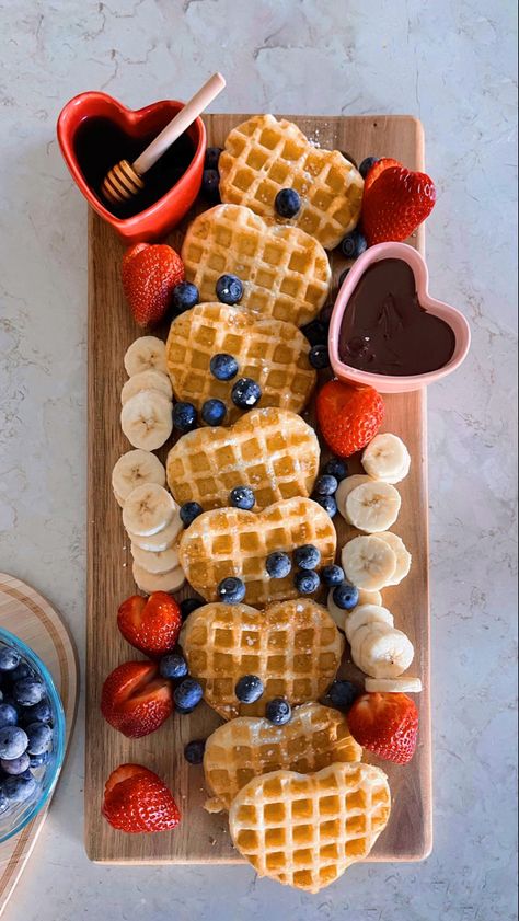 Brunch board with heart-shaped, golden waffles topped with powdered sugar, blueberries, bananas, and strawberries with syrup and nutella in heart-shaped containers. Birthday Waffles Breakfast, Valentines Waffles, Valentines Dessert, Candy Charcuterie, Brunch Board, Valentines Breakfast, Halloween Breakfast, Waffle Bar, Quirky Cooking