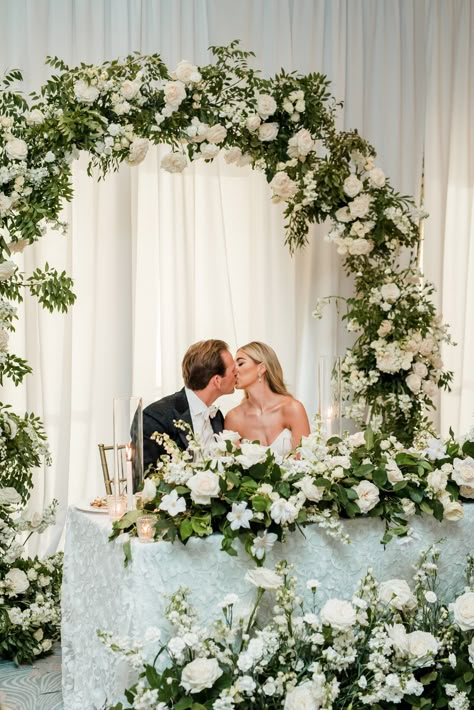 White florals and lush greenery were mixed together to create the ultimate sweetheart table arch backdrop. | John Myers Photography Flower Sweetheart Table Wedding, Flower Arch Wedding Reception, Greenery Wedding Backdrop Receptions, Wedding Table Arch, Bride And Groom Table Flower Arrangement, Sweetheart Table Wedding Arch, Bridal Head Table Ideas, Wedding Arch Sweetheart Table, Sweetheart Table With Arch