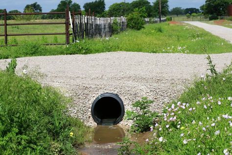 If you are observant enough, when you walk on a bridge, you may notice a small rectangular or square structure beneath the bridge as you pass through. That structure is called a culvert and is an essential component responsible for ensuring the smooth flow of water under roads and trails. You may not be aware of this, but there are distinct types of culverts, each with its purpose. This article will discuss everything you need to know about culverts, whether you're in construction or just ... Sloped Driveway Drainage Solutions, Diy Culvert Ideas, Driveway Culvert Ideas, Culvert Landscaping Ideas Drainage Ditch, Culvert Landscaping Ideas, Culverts Ideas, Driveway Culvert, Rock Drainage, Water Erosion