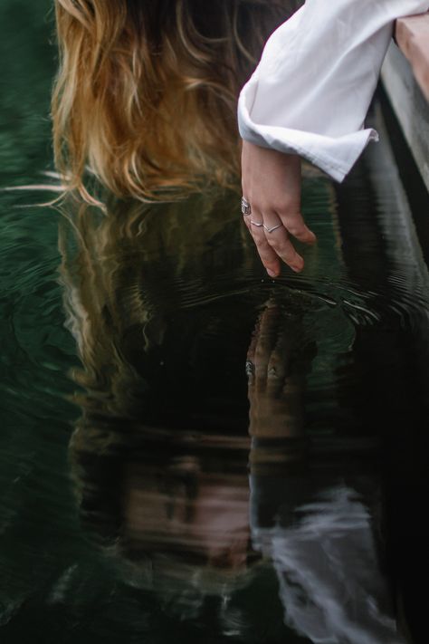 Moody portrait of a hand with rings reaching down towards water ripples. The reflection show the woman's face looking down toward the water while the tips of her hait lightly float on the water's surface. This shot was taken at the Sleepy Hollow Inn in Huntington, VT Woman Reflection In Water, Reflection In Water Photography, Dark Cottage Core Photoshoot, Looking Into Water Reflection, Water Reflection Photoshoot, Face Reflection In Water, Walking On Water Photography, Pirate Paladin, Water Portrait Photography