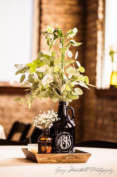 Growlers and Red Stripe wedding centerpieces. Baby's breath and eucalyptus decor Brewery Centerpieces, Hops Centerpiece Wedding, Growlers Wedding Decor, Wedding Growler Centerpiece, Brewery Table Decor, Brewery Bridal Shower Decorations, Brewery Shower Ideas, Brewery Wedding Centerpieces, Diy Simple Wedding Centerpieces