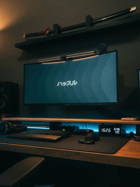 A moody desk setup illuminated by ambient lighting, featuring a monitor displaying Japanese characters, and decorative samurai swords on a shelf above. The workspace includes a mechanical keyboard, speakers, and a monitor light bar, creating a unique blend of modern technology and traditional Japanese decor. Setup Minimalist, Minimalist Desk Setup, Aesthetic Desk Setup, Minimal Workspace, Positive Environment, Dream Desk, Aesthetic Desk, Desktop Setup, Minimalist Desk