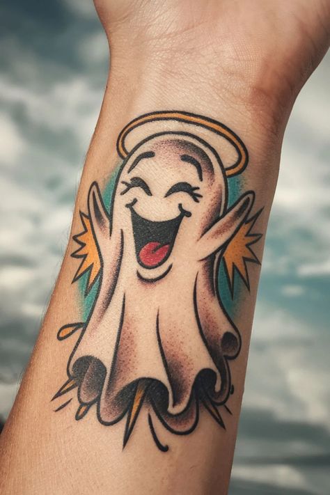 Colorful tattoo of a smiling ghost with a halo and wings on a person's forearm. Ghost Tattoos, Ghost Tattoo, Spooky Tattoos, Halloween Tattoo, Wrist Tattoos For Women, Spooky Ghost, The Supernatural, Hauntingly Beautiful, Halloween Tattoos