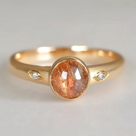 **Capture the warmth of the sun with our exquisite engagement ring, featuring a radiant sunstone at its center with two accent diamonds on either side. *Gem - 7.5mm round Sunstone Finish: Brushed finish *Gems: The natural gems natural hues vary, adding an organic touch to your ensemble. I'll try to select them in the spectrum as close to the picture as possible. Want to see your specific stone? Just send me a message, and I'll happily provide photos for you to choose from. *Metal: Delicately cra Sunstone Engagement Ring, Gold Leaf Ring, Earings Jewelry, Sunstone Ring, Unique Gold Rings, Sunstone Jewelry, Gold Leaf Rings, It Will Happen, Ring Inspo