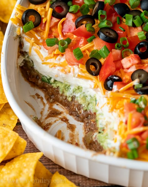 7 Layer Bean Dip with scoop taken out to show layers of beans, guacamole, sour cream and cheese. Black Bean Layer Dip, Halloween Nacho Dip, Easy Birthday Food Ideas, 7 Layer Bean Dip Recipe, Recipe With Refried Beans, Layered Nacho Dip, Layered Bean Dip Recipe, Layered Salads, Seven Layer Taco Dip