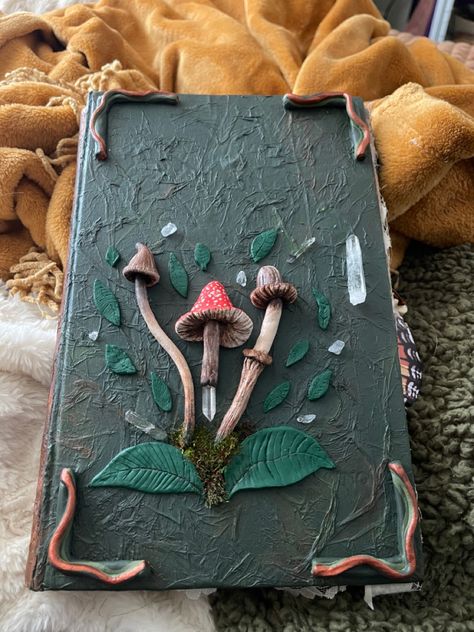 A green grimoire with clay mushrooms and crystals on the front cover. Alter Book Ideas, Grimoire Aesthetic Cover, Whimsigoth Journal, Grimoire Cover Ideas, Diy Grimoire Cover, Polymer Clay Journal Covers, Grimoire Book Cover, Grimoire Ideas Cover, Clay Book Cover