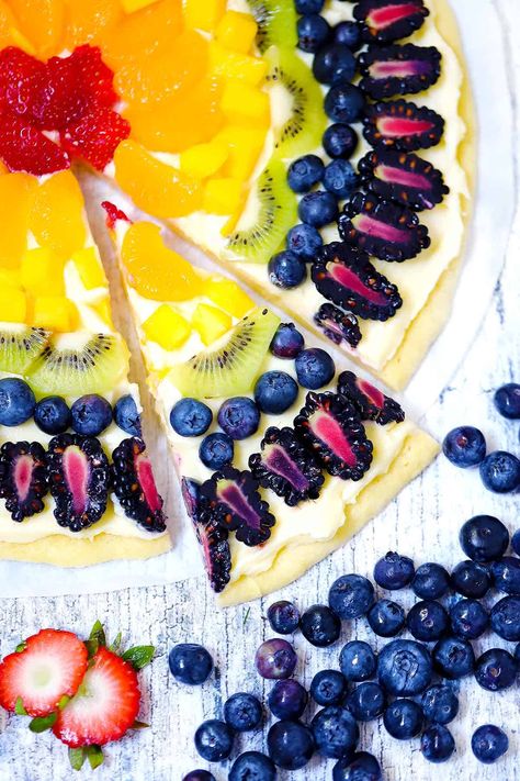 Rainbow Fruit Pizza is a great recipe to celebrate Pride with natural rainbow colors in healthy fruit! A sugar cookie crust is topped with cream cheese frosting and topped with fruit in all the colors of the rainbow for this easy and delicious make ahead dessert recipe that is great for parties, potlucks, or pride celebrations. Fruit Rainbow Cake, Sugar Cookie Fruit Pie, Pride Baking, Rainbow Fruit Tart, Rainbow Fruit Pizza, Pride Recipes, Pride Desserts, Italian Rainbow Cookie Cake, Easy Fruit Pizza Sugar Cookie