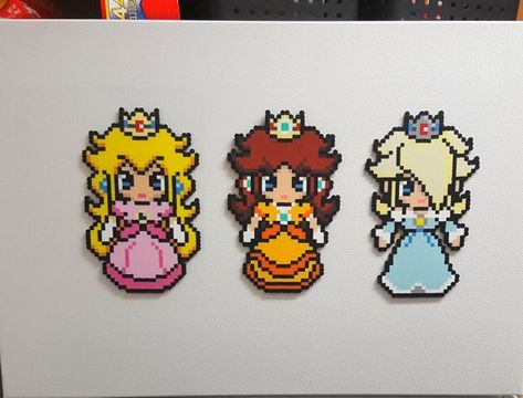 Peach, Daisy, and Rosalina are a trio of princesses that are waiting for you to take them home. Click the Add to Cart button now and look fabulous while you oversee the Mushroom Kingdom and spend the day with your favorite mustachioed plumbers. Impress your friends and family with your very own set of princesses - collect all 3! Young imaginations will love playing with them and cooking up all kinds of fun.Try placing one, two, or all three princesses on your locker, fridge, or door. You could m Daisy Super Mario, Peach Daisy And Rosalina, Daisy And Rosalina, 8 Bit Pixel Art, Princess Rosalina, Perler Bead Designs, Perler Bead Mario, Perler Beads Ideas, Hamma Beads Ideas