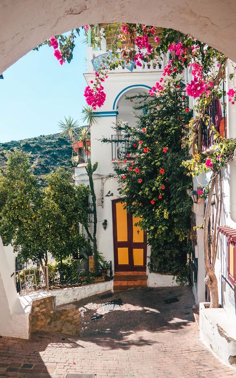 A white house with blue trims and a yellow and brown door, covered in Bougainvillea and Hibiscus flowers framed by a white arch in Mojácar Old Town, Spain. Spain Aesthetics, Spain Bucket List, Street Architecture, Spain Aesthetic, Spain Travel Guide, Andalucia Spain, Europe Summer, Spain And Portugal, Andalusia