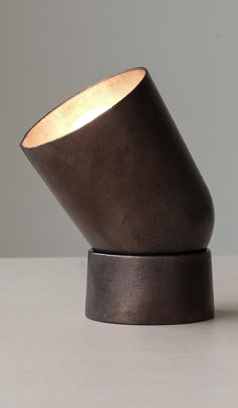 Substantial, architectural table lamp with cylindrical, rounded base and large, cup shaped shade. Articulated shade can be pivoted to direct light where it is needed. Made of solid, blackened sand cast bronze. Emits soft ambient light that reflects back onto the metal surface. Patinated bronze will continue to subtly darken over time with use, and can be restored to its original state with a polishing cloth. 8" tall when positioned fully upright, 5.16" Ø base. 10 foot black cloth cord with in li Waterfront Apartment, Henry Wilson, Waterfront Apartments, Sand Casting, Metal Surface, Spot Light, Ambient Light, Glass Art Sculpture, Glass Material