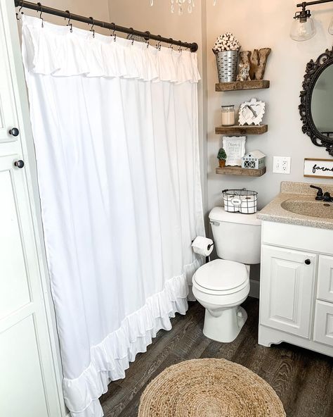 A simple white shower curtain showcases an elegant ruffled layer along the top and bottom portion of the curtain. Complete the vintage look with a set of wood floating shelves, a woven jute mat, and a steampunk vanity light over an antique black framed wall mirror. Modern Farmhouse Bathroom Decor, Lace Shower Curtains, Shabby Chic Shower, Shabby Chic Shower Curtain, Elegant Shower Curtains, Instagram Bathroom, Ruffle Shower Curtains, Farmhouse Bathroom Decor Ideas, Restroom Decor