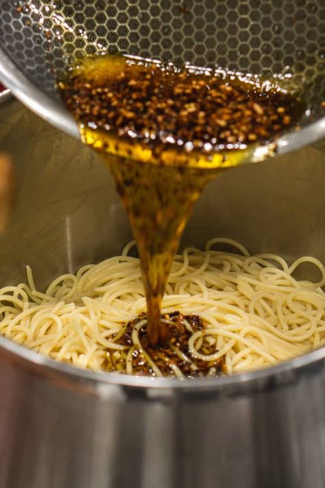 adding spice-infused olive oil to spaghetti pasta to make spicy spaghetti aglio e olio