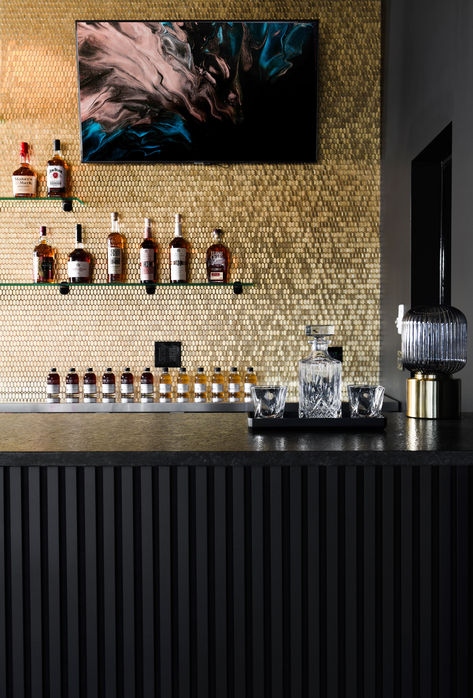 Where Opulence Meets Elegance: Our bar design is a harmonious fusion of timeless luxury and modern sophistication. The shimmering gold mosaic tiles on the wall radiate warmth and style, while the sleek black wood slats panel and black stone countertop at the front create a bold and inviting focal point. Cheers to a space that defines refined indulgence. Wood Slat Bar Design, Bar Cladding, Black And Gold Bar, Masculine Bar, Gold Mosaic Tile, Bar Concept, Restaurant Counter, Indoor Golf, Gold Tile