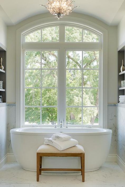 Freestanding oval tub under arched windows in a transitional master bathroom boasting a bathtub bench atop marble floor tiles. Bath Under Window, Bathtub Bench, Oval Tub, Arch Windows, Marble Floor Tiles, Oval Bathtub, Luxury Master Bathrooms, Bloxburg Modern, Bathtub Design