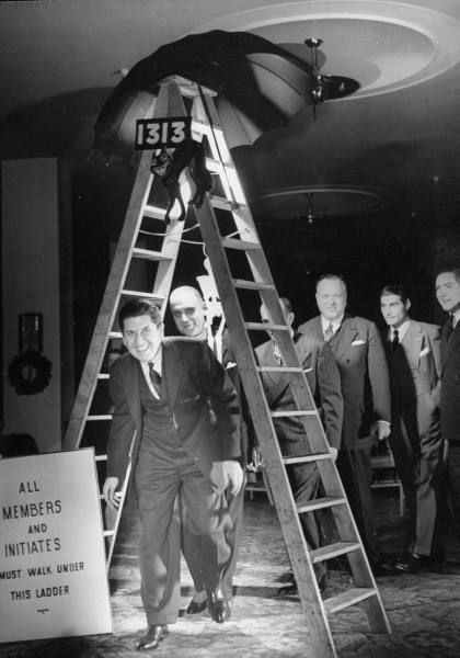 Members of the anti-superstition party walking underneath a bad luck ladder. Notice the umbrella opened, the number 13 twice, a black cat and a sign stating everyone must walk under this ladder. Superstitions Art, Friday The 13th Party, Friday The 13th Superstitions, 1940s Photos, Happy Friday The 13th, 13th Birthday Parties, Retro Horror, Snapchat Picture, Time Life