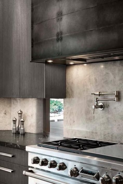 A black metal range hood is flanked by dark gray modern cabinets mounted in front of windows. Kitchen Island Hood Ideas, Mountain Modern Kitchen, Modern Kitchen Hood, Modern Metal Kitchen, Modern Range Hood, Kitchen Hood Ideas, Metal Range Hood, Kitchen Hood Design, Metal Cabinets