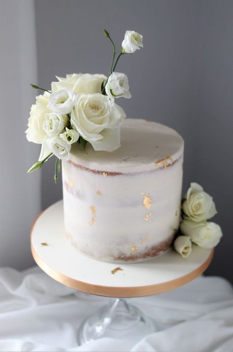 A white one tier semi-naked butttercream wedding cake decorated with cream roses and white lisianthus and flecks of edible gold leaf. Edged in gold ribbon and displayed on a clear glass cake stand. Elegant Intimate Wedding, Gold And White Cake, Wedding Cake With Fresh Flowers, Golden Birthday Cakes, Wedding Cake Simple Elegant, White And Gold Wedding Cake, Cake With Fresh Flowers, Gold Leaf Cakes, White Lisianthus